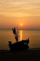 Silhouette of a fishing boat bound on a beach with sunrise in the morning, fresh orange sky. photo