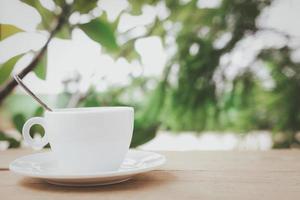 A white coffee cup with spoon in a cup and saucer are placed on a wooden plate and on the landscape nature background. photo