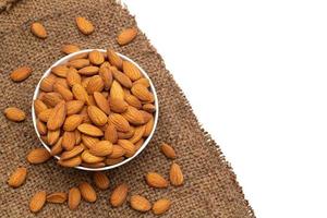 Almond nuts in white crockery with wooden spoon on brown sackcloth background,top view,flat lay,top down,selective focus. photo