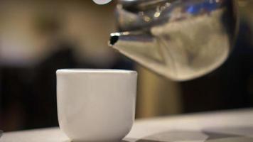 Pouring tea from metal pot to ceramic cup in Chinese restaurant video