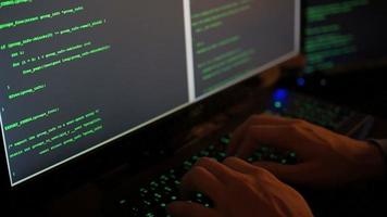 um hacker digita código verde na escuridão em várias telas