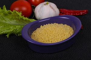 Raw couscous in the bowl served salad leaves, tomato and pepper photo