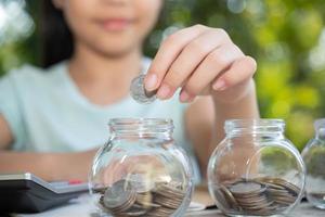 Cute asian little girl playing with coins making stacks of money,kid saving money into piggy bank, into glass jar. Child counting his saved coins, Children learning about for the future concept. photo