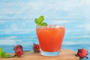 vaso de té de roselle helado con fruta fresca de roselle sobre una mesa de madera para un concepto de bebida herbal saludable. té orgánico de hierbas para una buena salud. foto