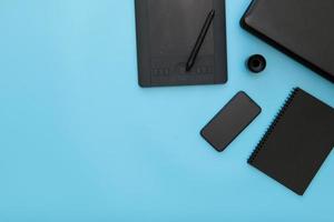 Workplace with notebook, pen graphics tablet, keyboard, smartphone, mouse pad, on work table. above view shot.  copy space on blue color background. photo