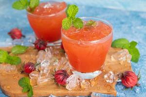 vaso de té de roselle helado con fruta fresca de roselle sobre una mesa de madera para un concepto de bebida herbal saludable. té orgánico de hierbas para una buena salud. foto