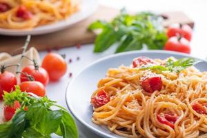 Tasty appetizing classic italian spaghetti pasta with tomato sauce, cheese parmesan and basil on plate and ingredients for cooking pasta on white marble table. photo