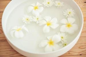 closeup of frangipani flowers and chrysanthemum floating in bowl of water at wellness center. white flowers in ceramic bowl with water for aroma therapy at spa. spa setting for beauty treatment. photo