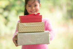 Christmas portrait of happy smiling little girl child with gift box near a green branch tree. green leaves bokeh out of focus background from nature forest. photo