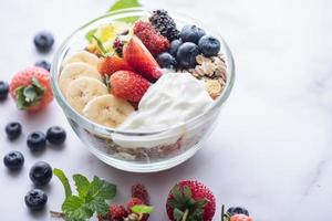 bowl of oat granola with yogurt, fresh blueberries, mulberry, strawberries, kiwi, banana, mint and nuts board for healthy breakfast, top view, copy space, flat lay. vegetarian food concept. photo