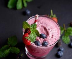 delicioso batido de fresa, mora y arándano adornado con bayas frescas y menta en vaso. enfoque suave. hermoso aperitivo frambuesas rosadas, bienestar y concepto de pérdida de peso. foto