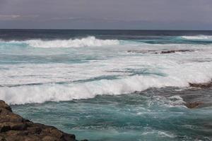 Turbulent ocean waves with white foam beat coastal stones photo