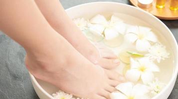 closeup view of woman soaking her feet in dish with water and flowers on wooden floor. Spa treatment and product for female feet and hand spa. white flowers in ceramic bowl. photo