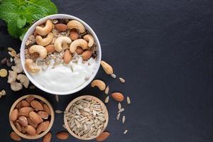 Homemade granola or muesli, bowl of oat granola with yogurt, almond, Cashew nuts, mint and nuts on the black rock board for healthy breakfast, copy space. Healthy breakfast menu concept. photo