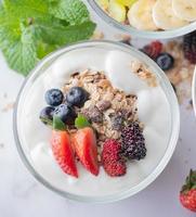 bowl of oat granola with yogurt, fresh blueberries, mulberry, strawberries, kiwi, banana, mint and nuts board for healthy breakfast, top view, copy space, flat lay. vegetarian food concept. photo