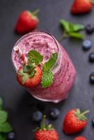 Delicious strawberry, mulberry and blueberry smoothie garnished with fresh berries and mint in glass. soft focus. beautiful appetizer pink raspberries, well being and weight loss concept. photo