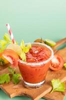 glass glass of tomato juice, lime with fresh bright bunch of tomatoes isolated on green background, green parsley. vegetable drink. photo