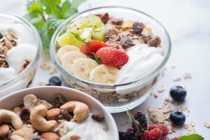 bowl of oat granola with yogurt, fresh blueberries, mulberry, strawberries, kiwi, banana, mint and nuts board for healthy breakfast, top view, copy space, flat lay. vegetarian food concept. photo