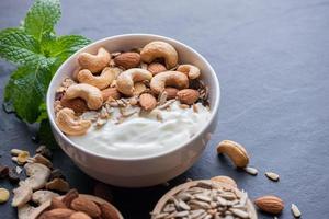 Homemade granola or muesli, bowl of oat granola with yogurt, almond, Cashew nuts, mint and nuts on the black rock board for healthy breakfast, copy space. Healthy breakfast menu concept. photo