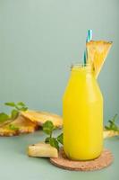 Pineapple cocktail or fresh pineapple juice, mint leaves in glass bottles with straws with ice and  pineapples on a green background. selective focus photo