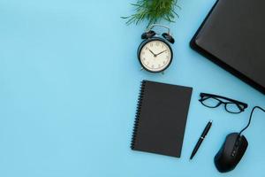 Creative flat lay design of workspace desk with laptop, alarm clock, blank notebook, stationery with blue copy space background. photo