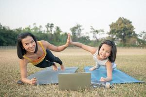 Mother and daughter doing yoga. woman and child training in the park. outdoor sports. healthy sport lifestyle, chaturanga pose. well being, mindfulness concept,watching video tutorial online on laptop photo