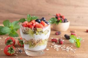 Homemade muesli, bowl of oat granola with yogurt, fresh blueberries, mulberry, strawberries, kiwi, mint and nuts board for healthy breakfast, copy space. Healthy breakfast concept. Clean eating. photo