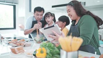 familjeperson som använder digital surfplatta för att lära sig laga mat i köket, barndotter med mamma och pappa livsstil hemma tillsammans, färsk grönsakssallad och måltid för att lära sig att göra meny video