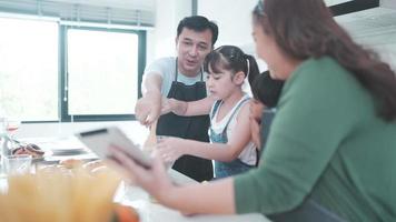 pessoa da família usando tablet digital para aprender a cozinhar uma comida na cozinha, filha criança com estilo de vida de mãe e pai em casa juntos, salada de legumes fresca e refeição para aprender a fazer menu video