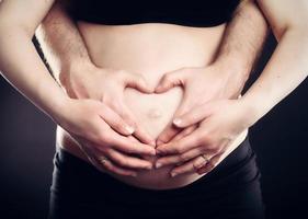 A couple touching belly in a heart shape. photo