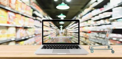 supermarket aisle blurred background with laptop computer and cart on wood table online shopping concept photo