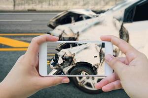 mujer que usa un teléfono inteligente toma una foto de un accidente automovilístico en la carretera
