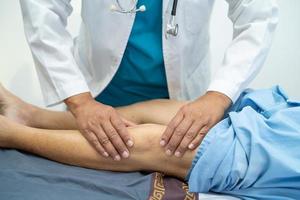 médico asiático fisioterapeuta que examina, masajea y trata la rodilla y la pierna del paciente mayor en el hospital de enfermería de la clínica médica ortopedista. foto