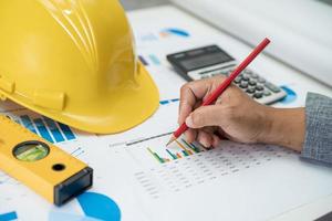 Asian engineer with plan project blueprint, graph and yellow helmet and engineering construction tools. photo