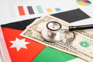 estetoscopio negro sobre fondo de bandera jordana con concepto de gráfico, negocios y finanzas. fondo de bandera con billetes de dólar estadounidense, concepto de negocios y finanzas. foto