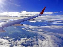 alas de avión durante el vuelo, vistas desde la ventana del pasajero hay muchas nubes blancas en el cielo azul foto