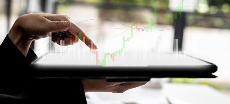 Person holding a tablet and pointing to a chart diagram showing a stock's up-and-down candlestick chart, graphically displayed on the tablet screen as an uptrend. Stock investor concept. photo