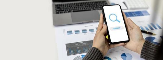 A woman holding a smartphone on a screen showing the text search and a magnifying glass, she is using the smartphone to search the Internet. Concept of using technology and the Internet. photo