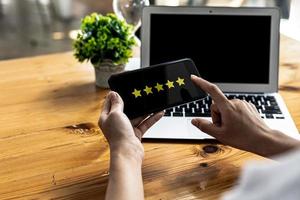 Person holding a smartphone with a screen showing 5 yellow stars, is reviewing a product through an online shopping application. Concept of using applications on smartphones via the Internet network. photo