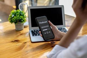 Person holding a smartphone in front of a podcast application display, using a smartphone to listen to podcasts over the Internet network. Concept of using smartphones, entertainment media and online. photo