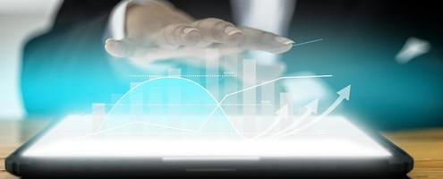 un hombre de negocios extiende sus manos en la pantalla de una tableta sobre una mesa, un paisaje gráfico en la pantalla que muestra un gráfico del estado financiero y una flecha que muestra el crecimiento. concepto de gestión empresarial rentable foto
