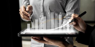 Two business people using a tablet to view company financial reports, graphics showing financial and numerical growth data. The concept of financial management to grow and be profitable. photo