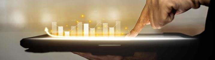 Person holding a tablet and pointing to a chart diagram showing a stock's up-and-down candlestick chart, graphically displayed on the tablet screen as an uptrend. Stock investor concept. photo