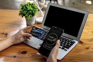 Person holding a smartphone in front of a screen showing an online shopping application, using the smartphone to make purchases and pay by credit card. Using a smartphone in online shopping concept. photo