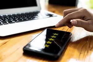 Person holding a smartphone with a screen showing 5 yellow stars, is reviewing a product through an online shopping application. Concept of using applications on smartphones via the Internet network. photo