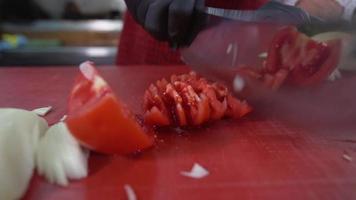 o cozinheiro está cortando o tomate. confecção de saladas. o cozinheiro está cortando o tomate para usar na salada. câmera lenta.