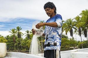 Fisherman preparing his net on the shore with palm trees in the background. photo