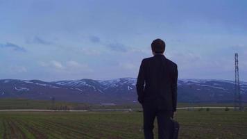 Businessman in suit and business bag walking in field. Businessman in suit with bag walking towards horizon. video