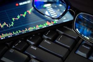 Stock market chart screen on keyboard computer and eyeglasses, online investment concept photo