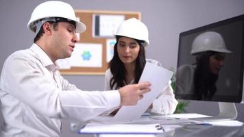 Engineers working on the project. Two white helmeted engineers are working on the project, which is angled on the computer at a table and is also on the papers. video